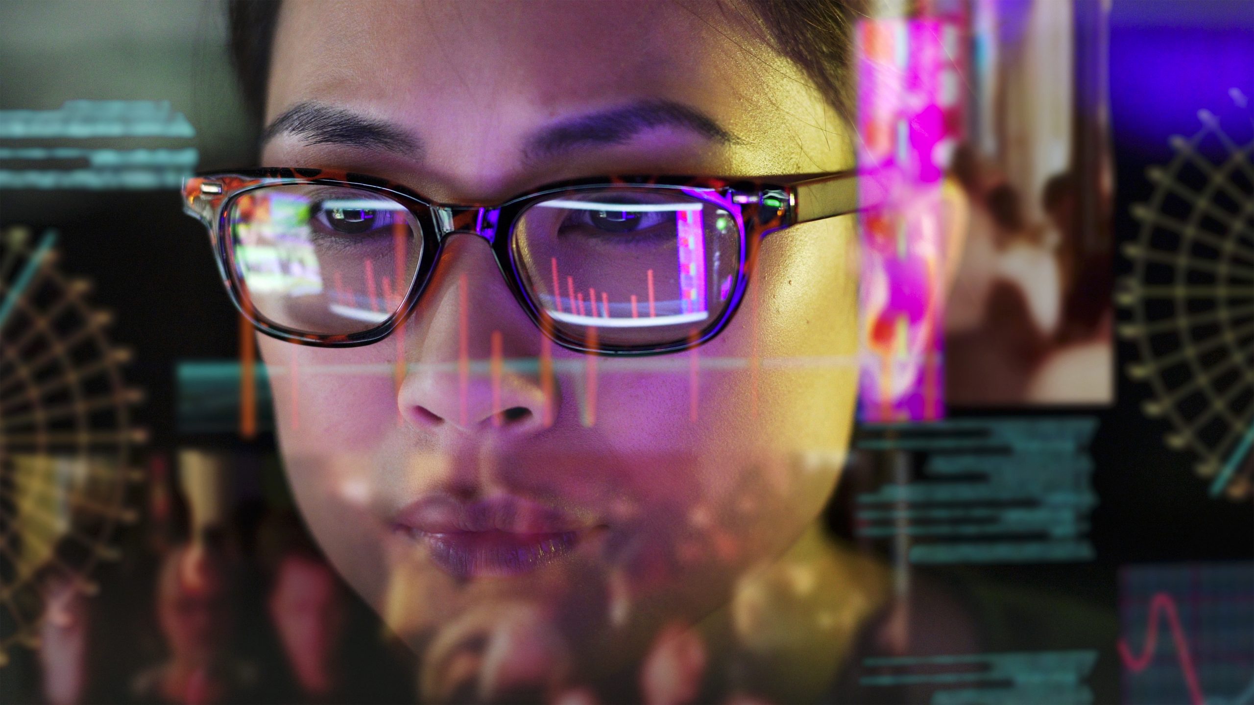 Close up stock photo of an Asian woman carefully studying moving data on her computer screen, the screen is unusual as it is transparent and the camera is looking through the back of the screen.