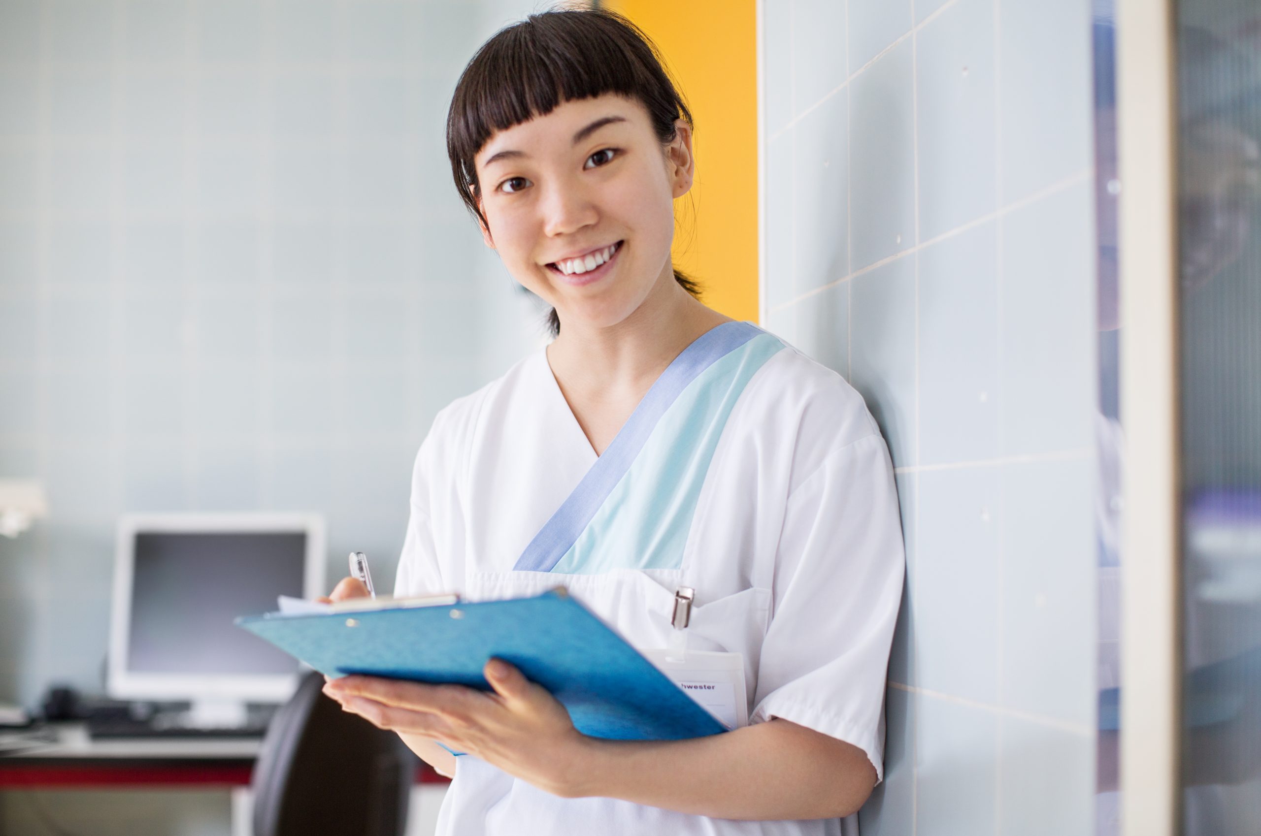 Female medical professional working in clinic holding clipboard and writing patient history. Smiling nurse writing medical report at hospital